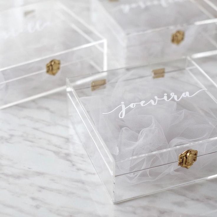 four clear boxes with gold handles and names on the lids are sitting on a marble surface