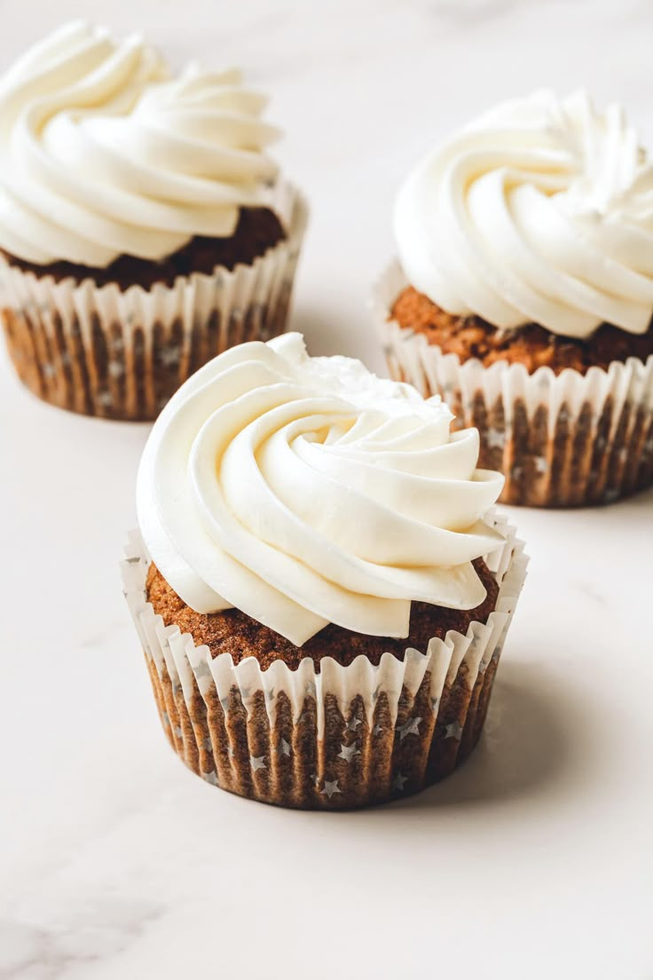 three cupcakes with white frosting sitting on top of a marble countertop