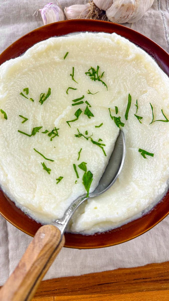 a bowl filled with mashed potatoes and parsley on top of a wooden table