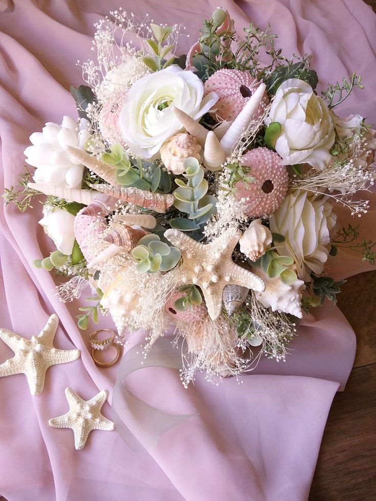 a bridal bouquet is laying on a pink blanket with starfishs and seashells