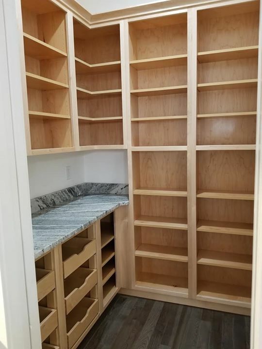 an empty walk in closet with wooden shelves and marble counter tops on one side, and wood shelving on the other