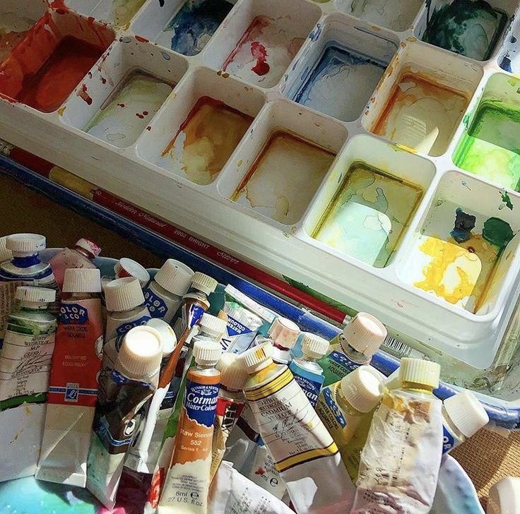 an assortment of paints and brushes sitting on top of a table next to a container