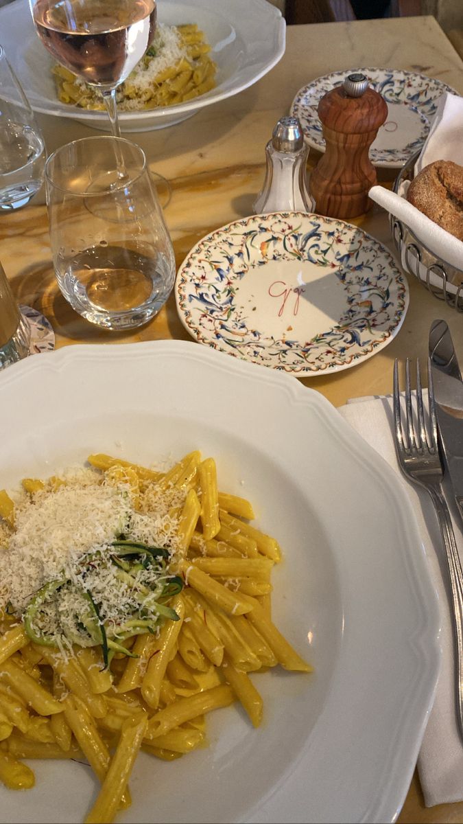 pasta with cheese and spinach on a white plate next to silverware, wine glasses and bread