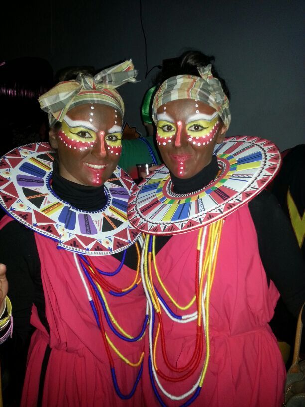 two women with painted faces and headdresses pose for the camera in front of a dark room