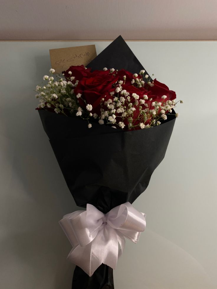 a bouquet of red roses wrapped in black paper and tied with a white ribbon on a wall