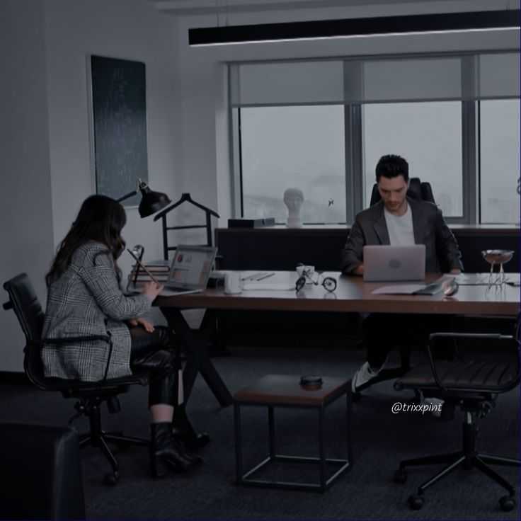 two people sitting at a table with laptops