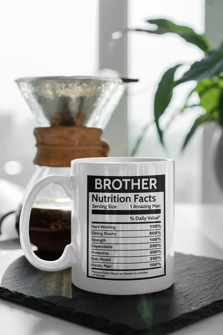 a white coffee mug sitting on top of a table next to a potted plant