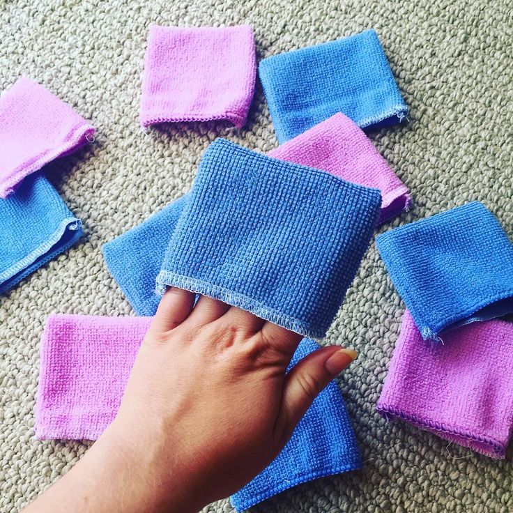 a hand is holding several pieces of blue and pink cloth on the floor next to each other