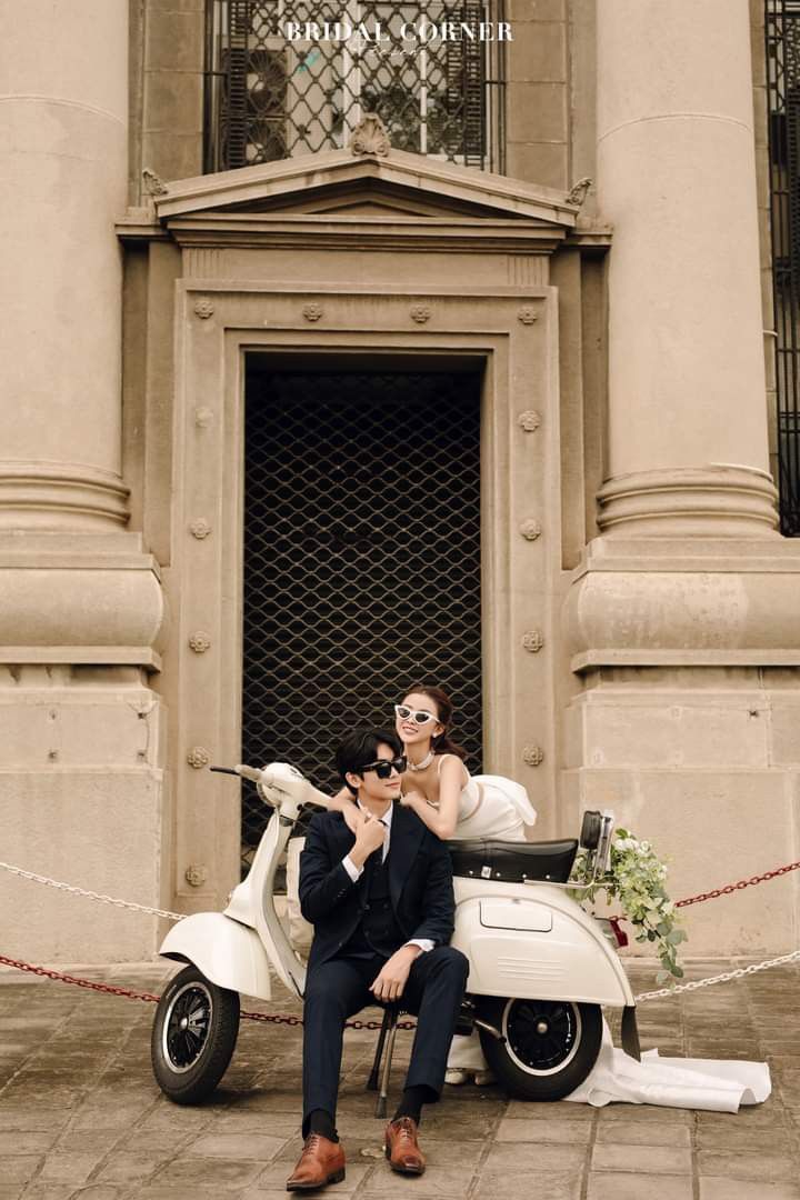 a bride and groom sitting on a scooter in front of an old building