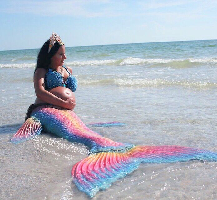 a woman sitting on top of a mermaid tail in the ocean next to the beach