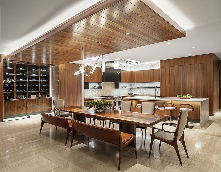 a large dining room table and chairs in front of a kitchen with wood paneling