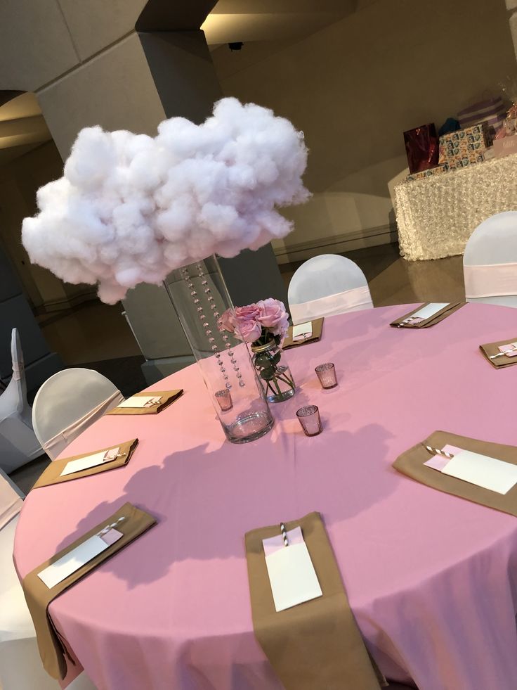 a pink table cloth topped with a vase filled with cotton floss and place cards