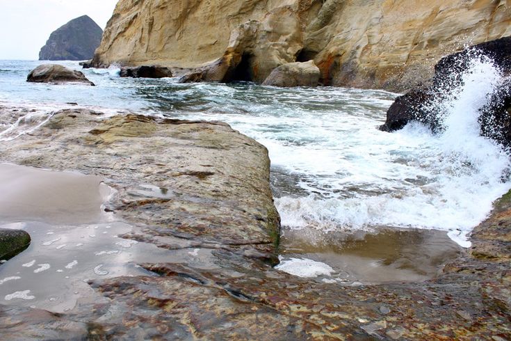 the water is splashing on the rocks by the beach