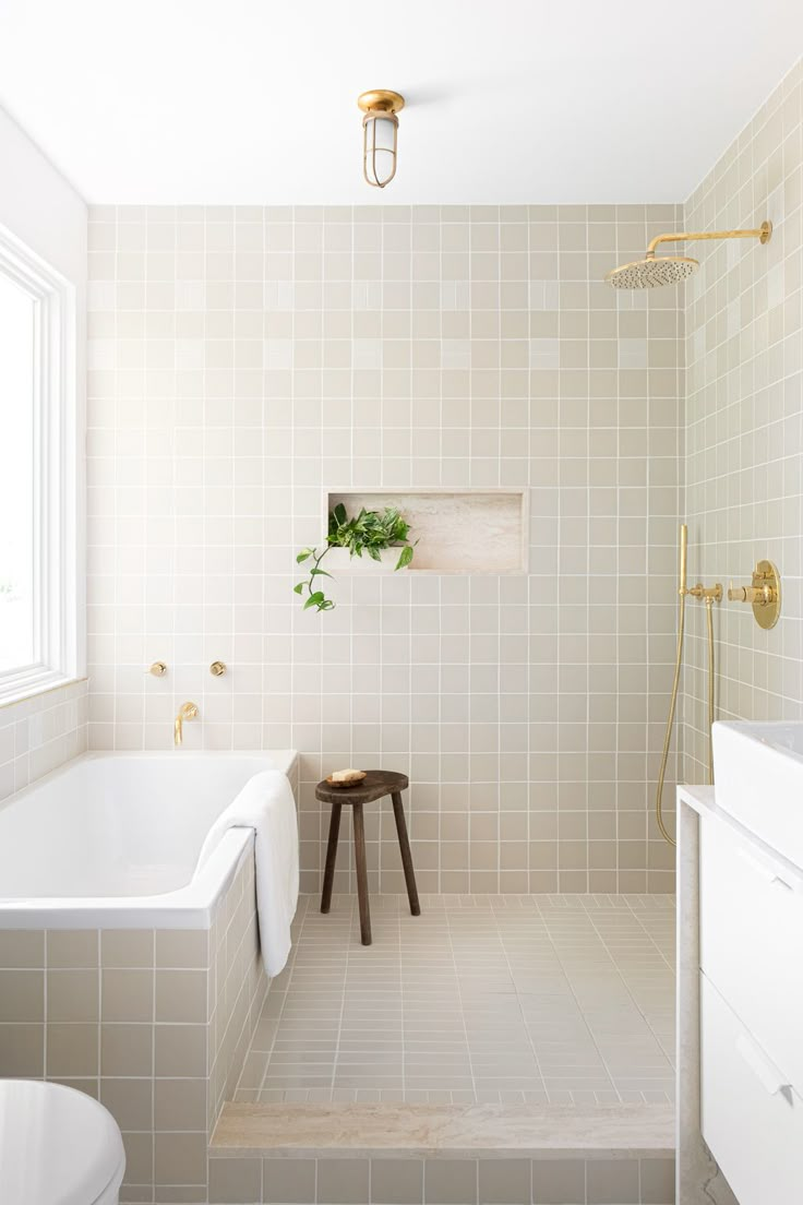 a white tiled bathroom with a stool next to the tub