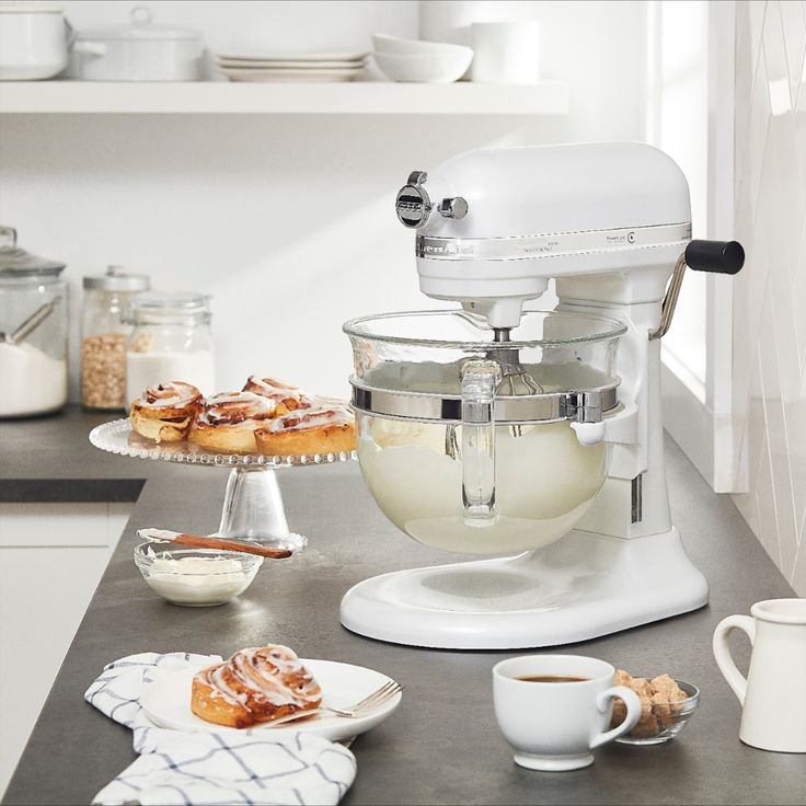 a white mixer sitting on top of a kitchen counter next to plates and cupcakes