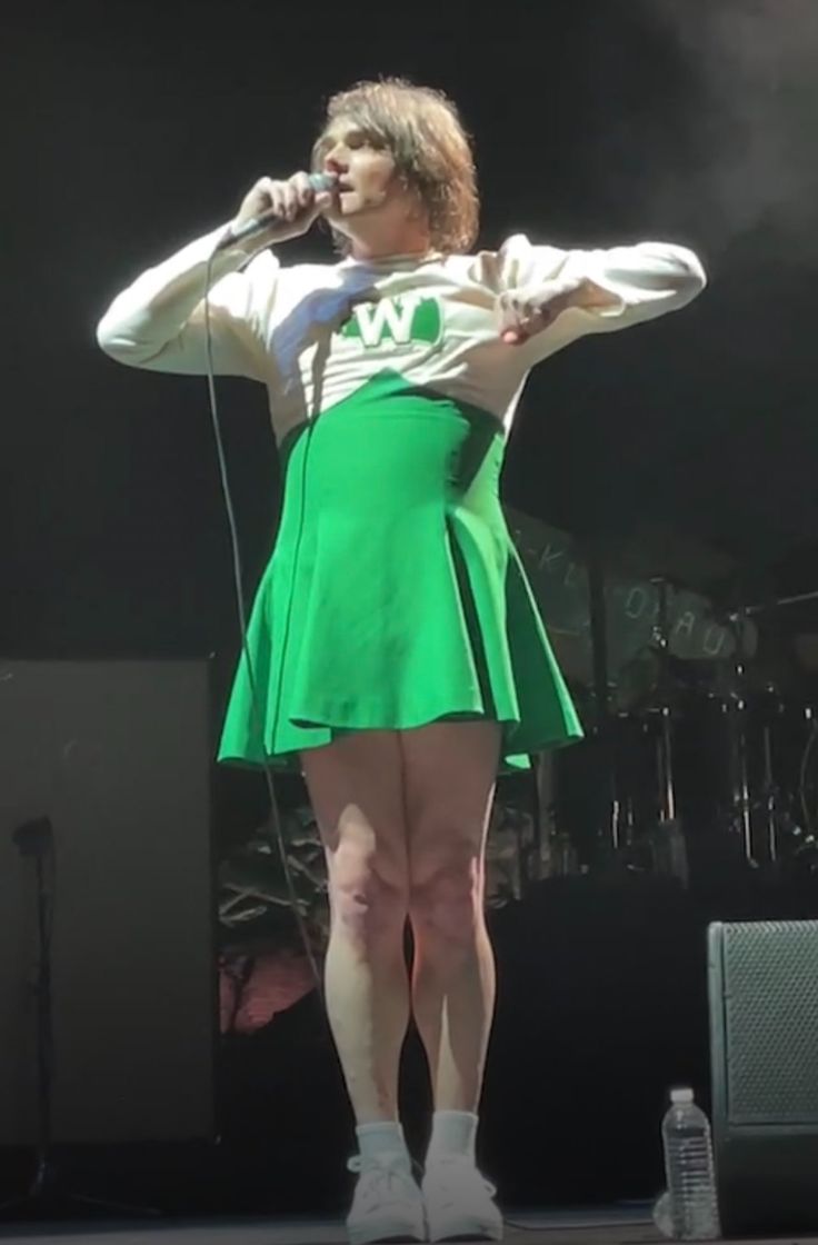 a woman in a green skirt on stage with a microphone and headphones to her ear