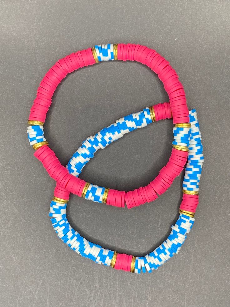 two pink and blue bracelets sitting on top of a gray table next to each other