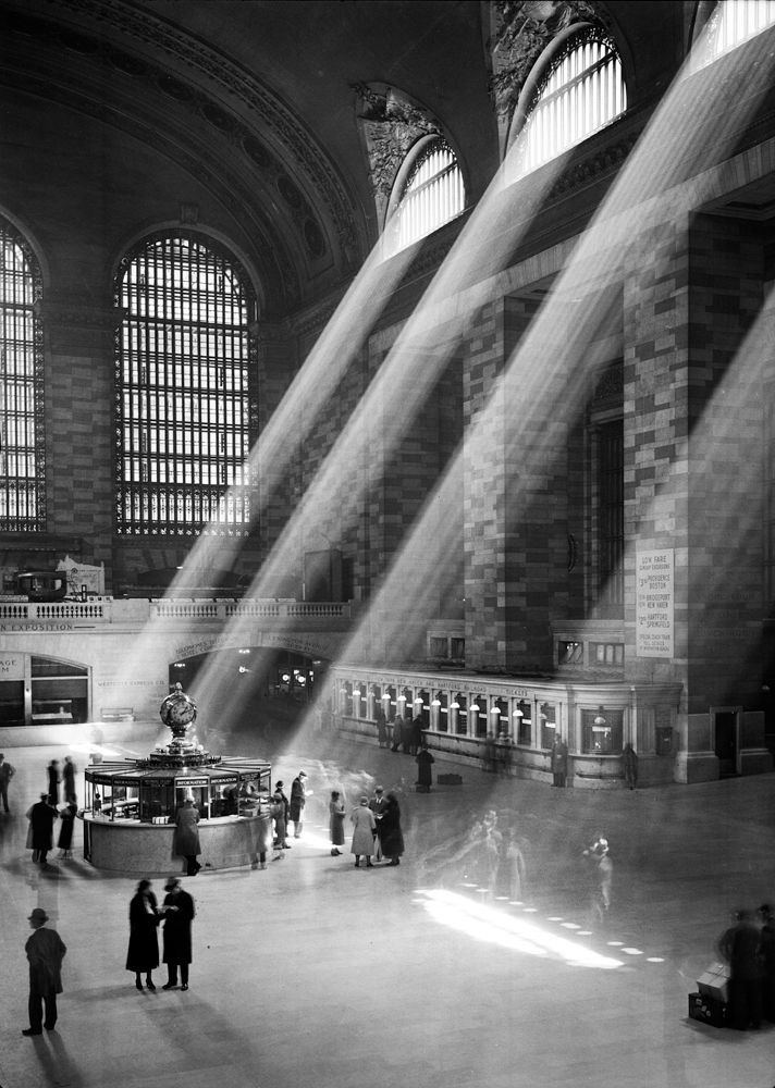 people are standing in an old train station with sunbeams shining through the windows