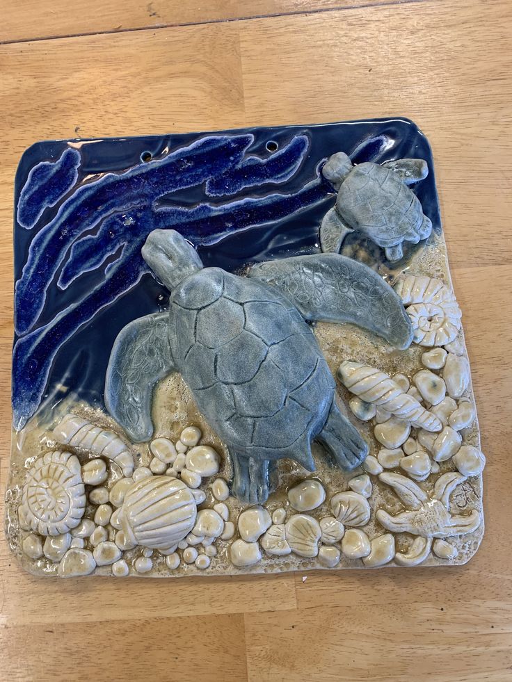 a glass tile with two sea turtles and shells on the bottom, sitting on a wood floor