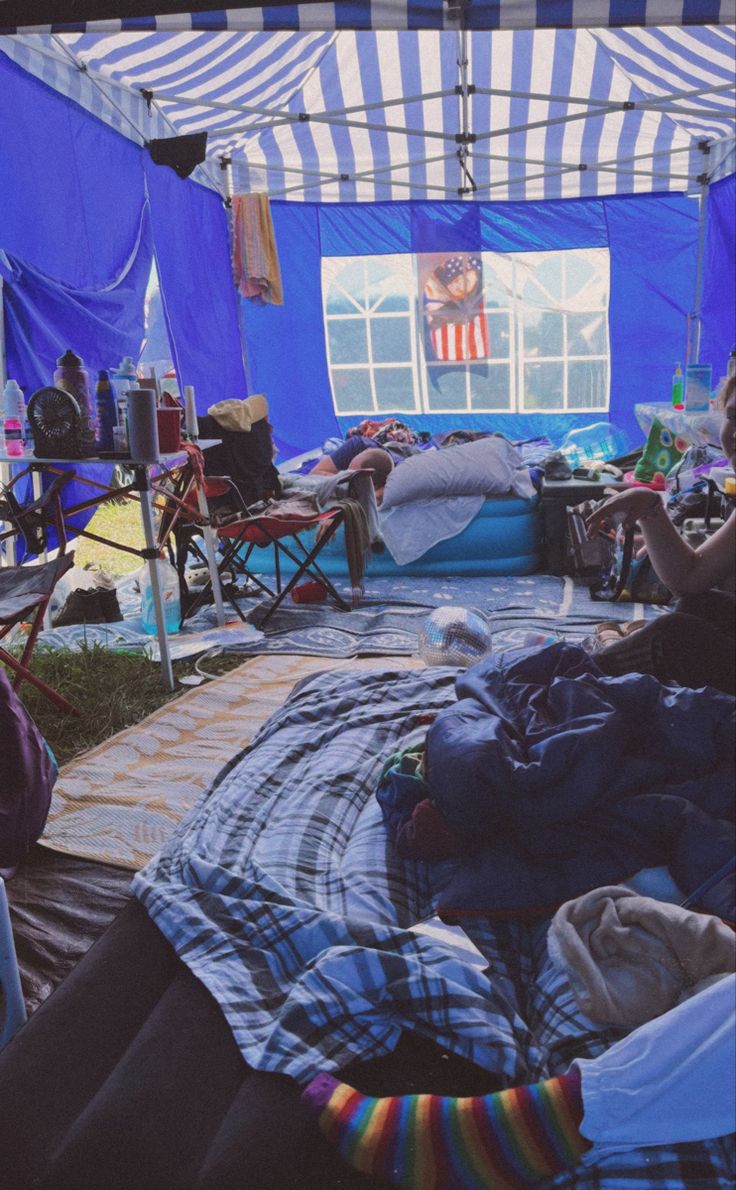 a group of people sitting in tents with blue tarps on the roof and one person laying down