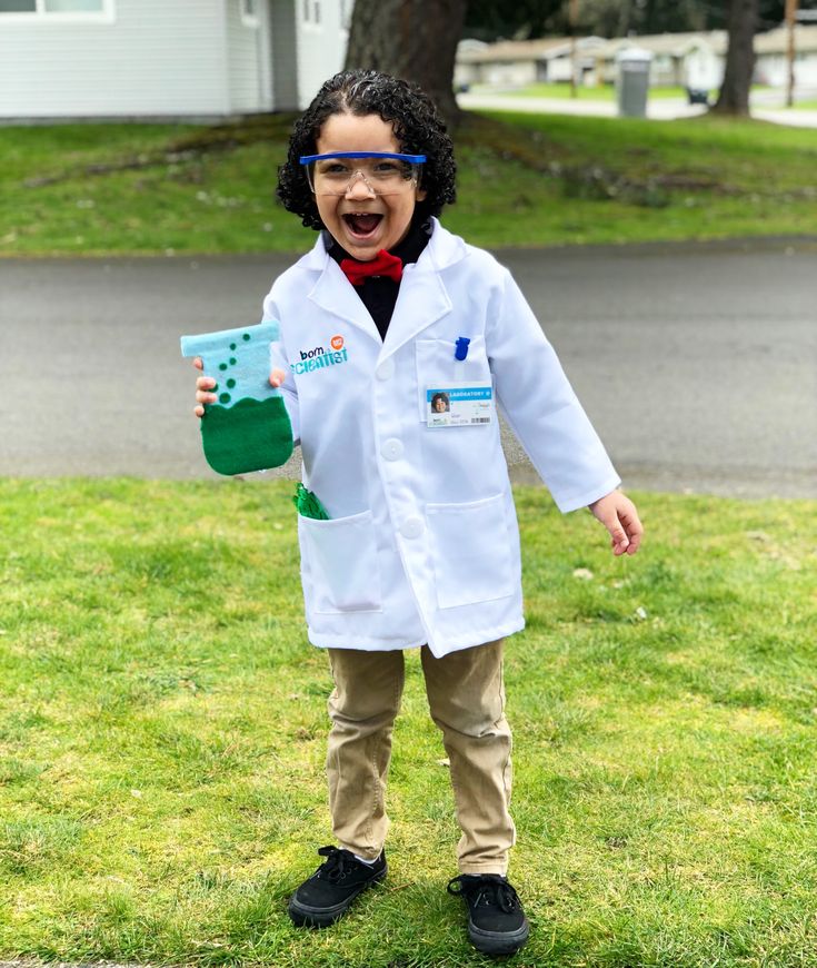 a young boy wearing a lab coat and glasses holding a green object in his hand