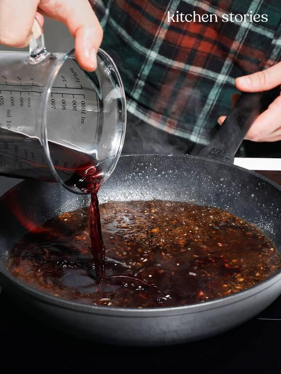 someone pouring red wine into a pan with food in it on top of the stove