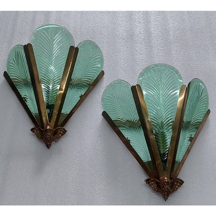 two green glass wall sconces with gold trimmings and leaves on them