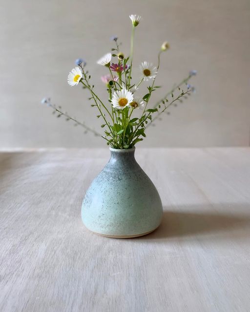 a vase with flowers in it sitting on a table top next to a white wall