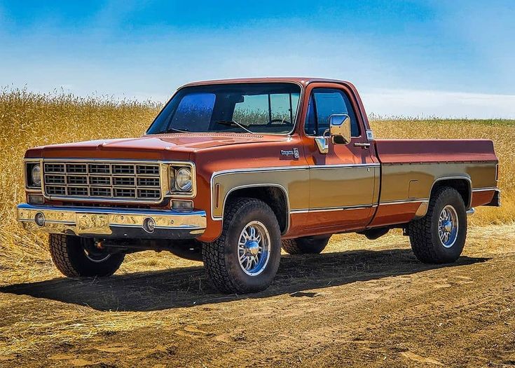 an orange and brown truck parked in the middle of a dirt road next to a field