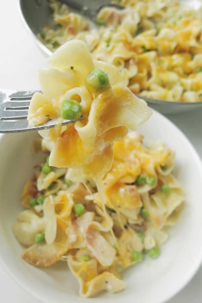 a fork full of pasta and peas on a white plate with another dish in the background