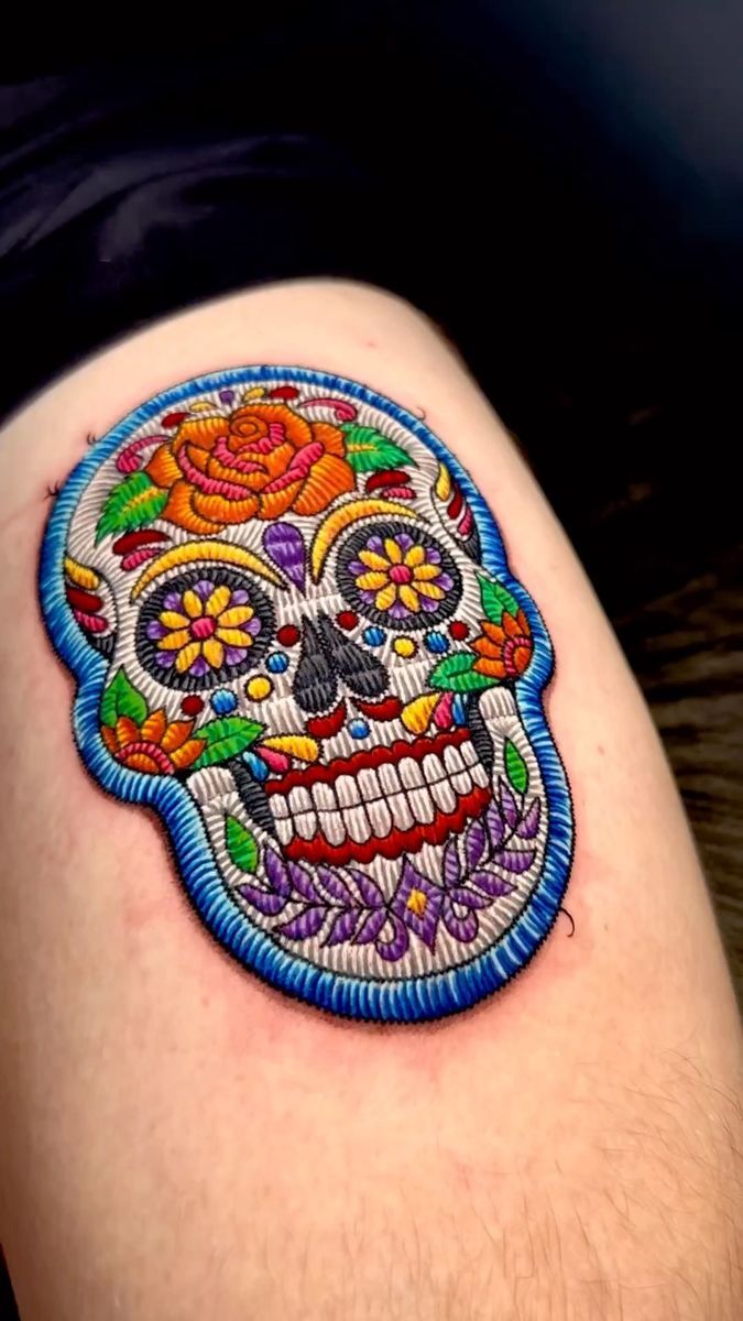 a person with a colorful tattoo on their thigh that has a skull and flowers on it