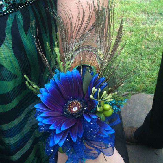 a woman's arm with a blue flower and peacock feathers on it, next to grass