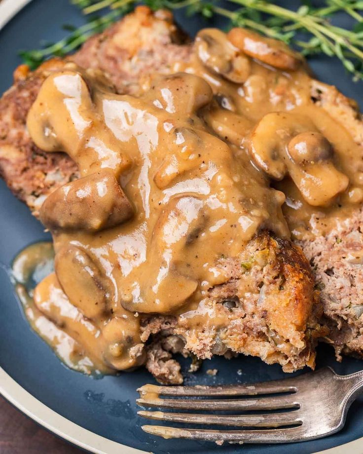 a blue plate topped with meatloaf covered in gravy next to a fork