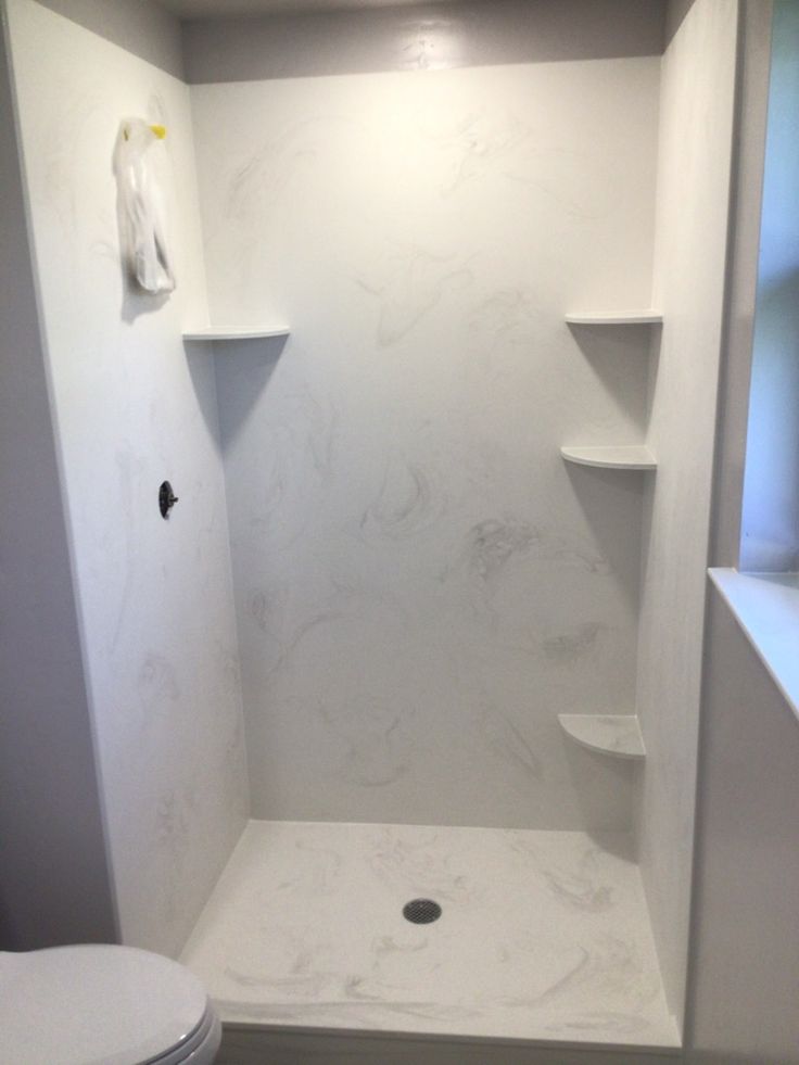 a white toilet sitting in a bathroom next to a walk in shower with shelves on the wall