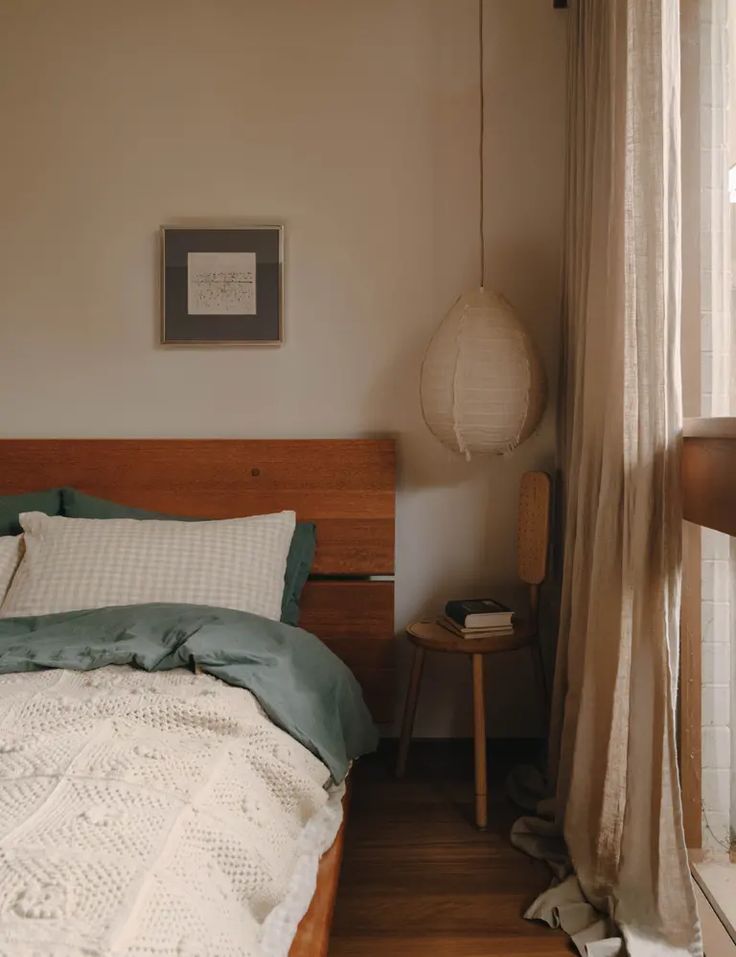 a bed sitting next to a window in a room with wooden floors and white curtains