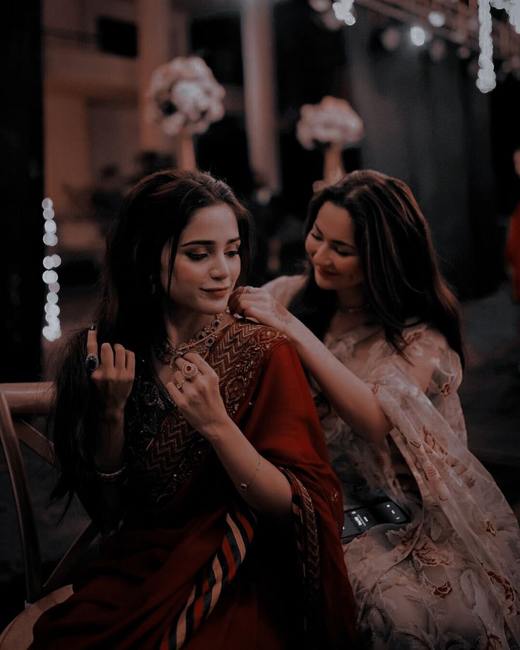 two beautiful women sitting next to each other in front of some lights on the ceiling