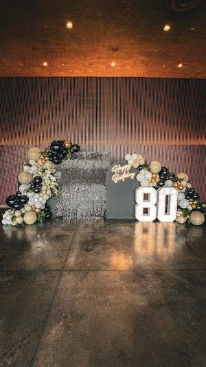 an arrangement of flowers and balloons is displayed on the floor in front of a sign that reads 80