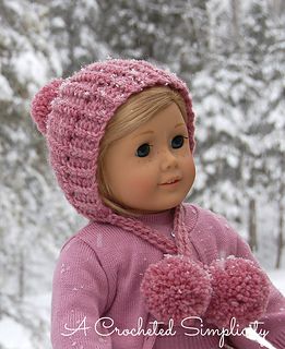 a doll wearing a knitted hat and mittens standing in the snow with trees behind it