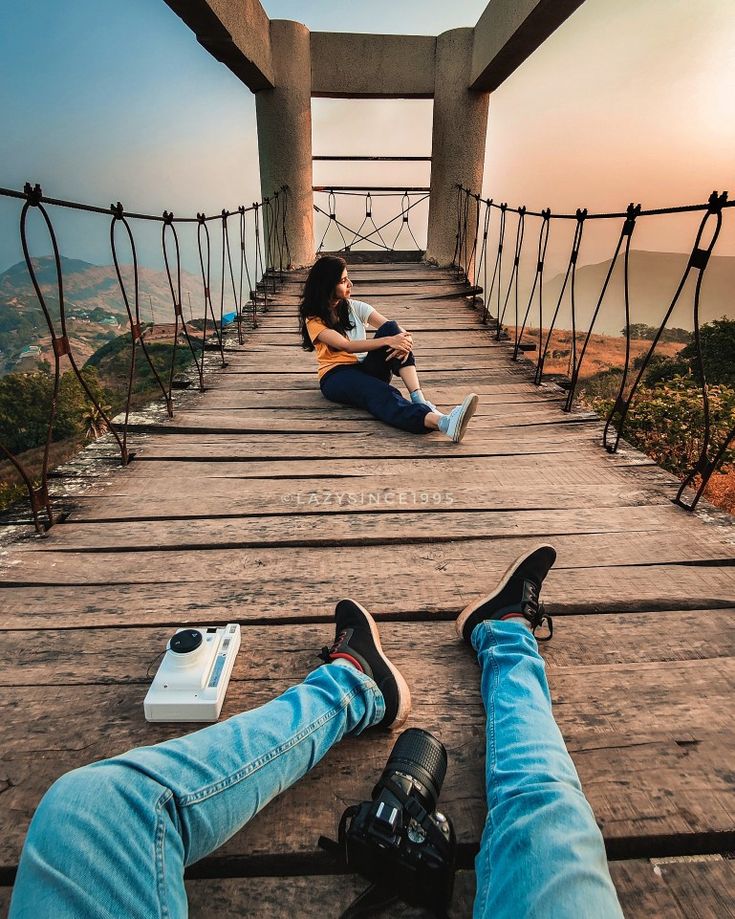 two people sitting on a bridge with their legs crossed and one person taking a photo