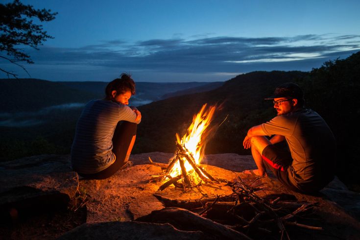 two people sitting around a campfire at night