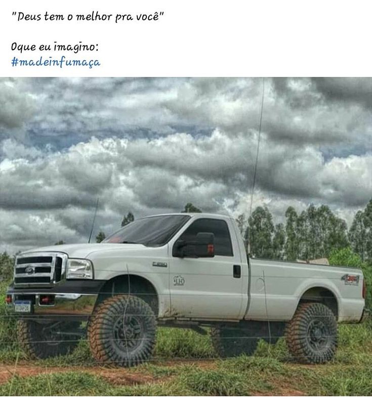 a white truck parked on top of a lush green field next to a sky filled with clouds