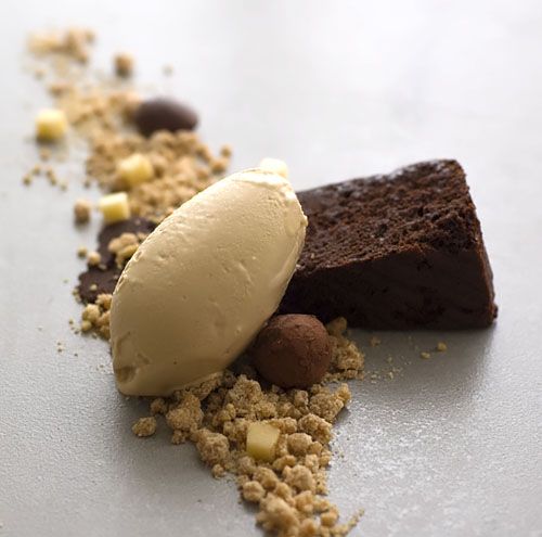 a piece of chocolate cake with ice cream and nuts on the side, sitting on a white surface