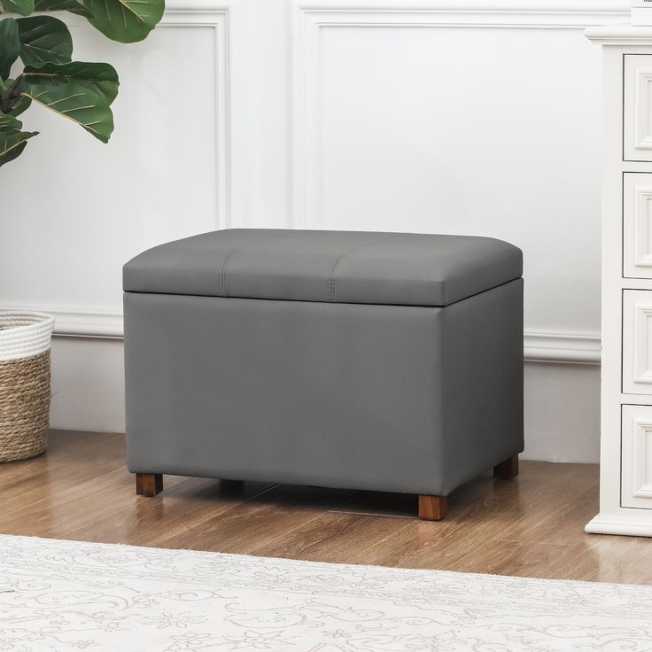 a grey storage bench sitting on top of a hard wood floor next to a plant