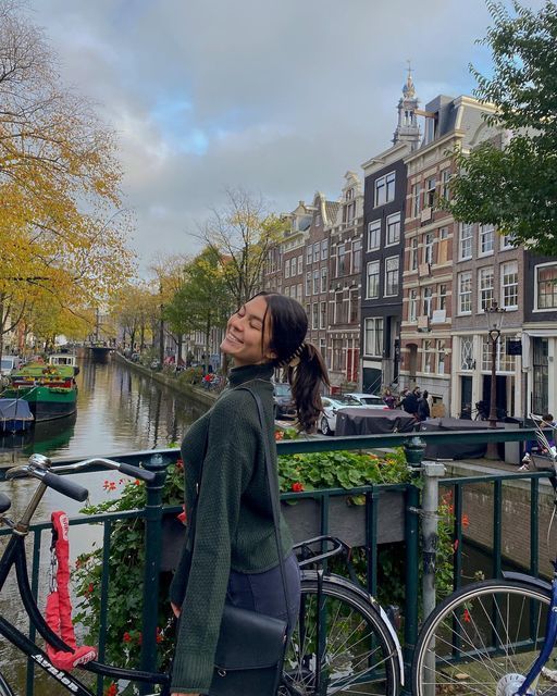 a woman standing next to a bike on a bridge over a canal in the city