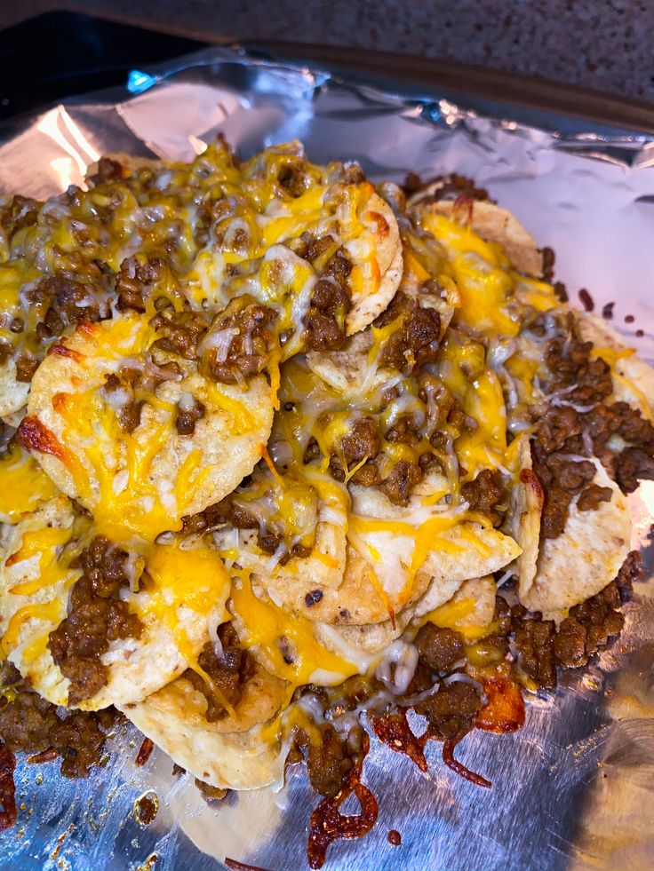 a pile of nachos sitting on top of foil covered in cheese and chili