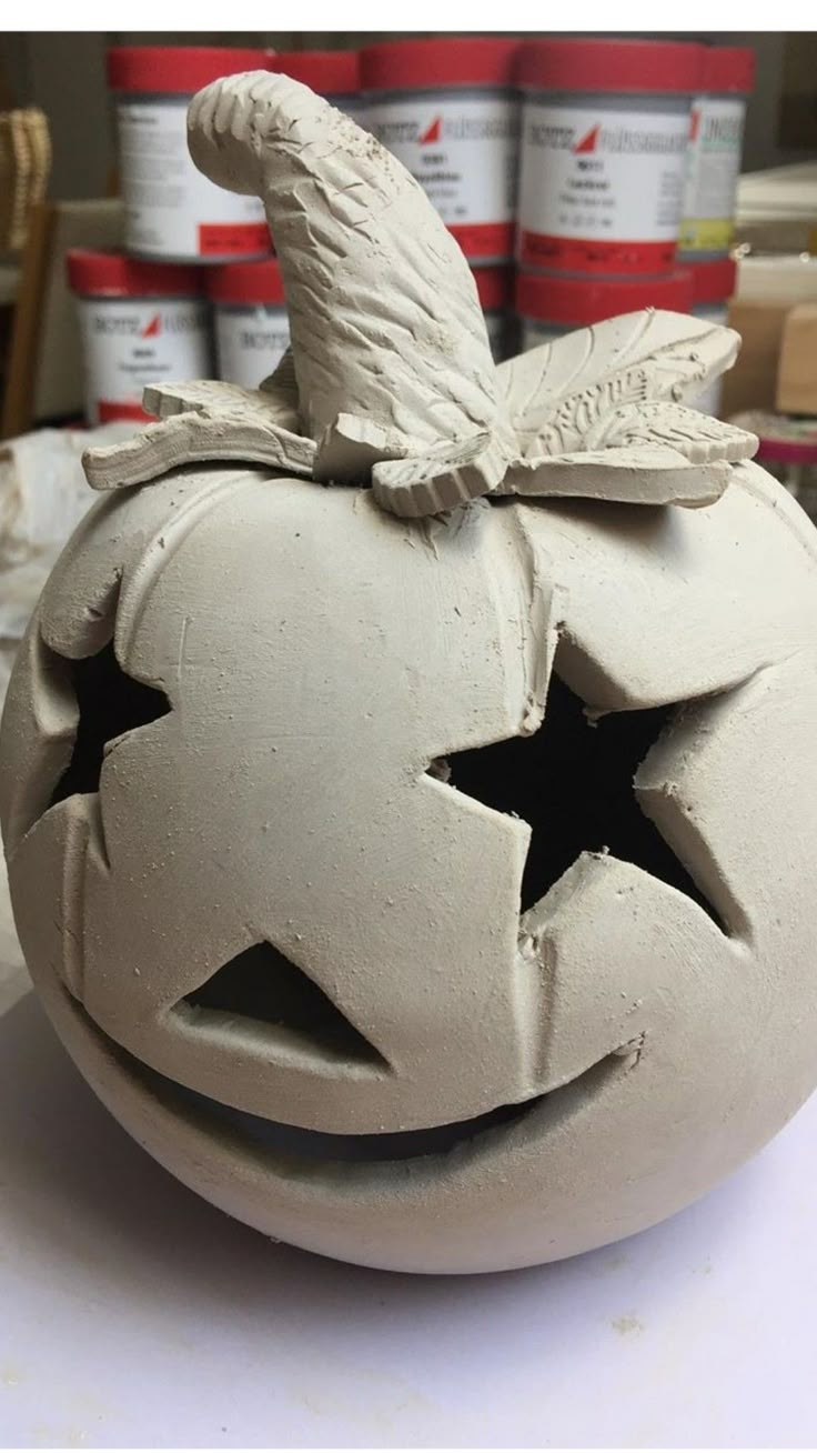 a clay pumpkin with a witches hat on it's head, sitting in front of some paint cans