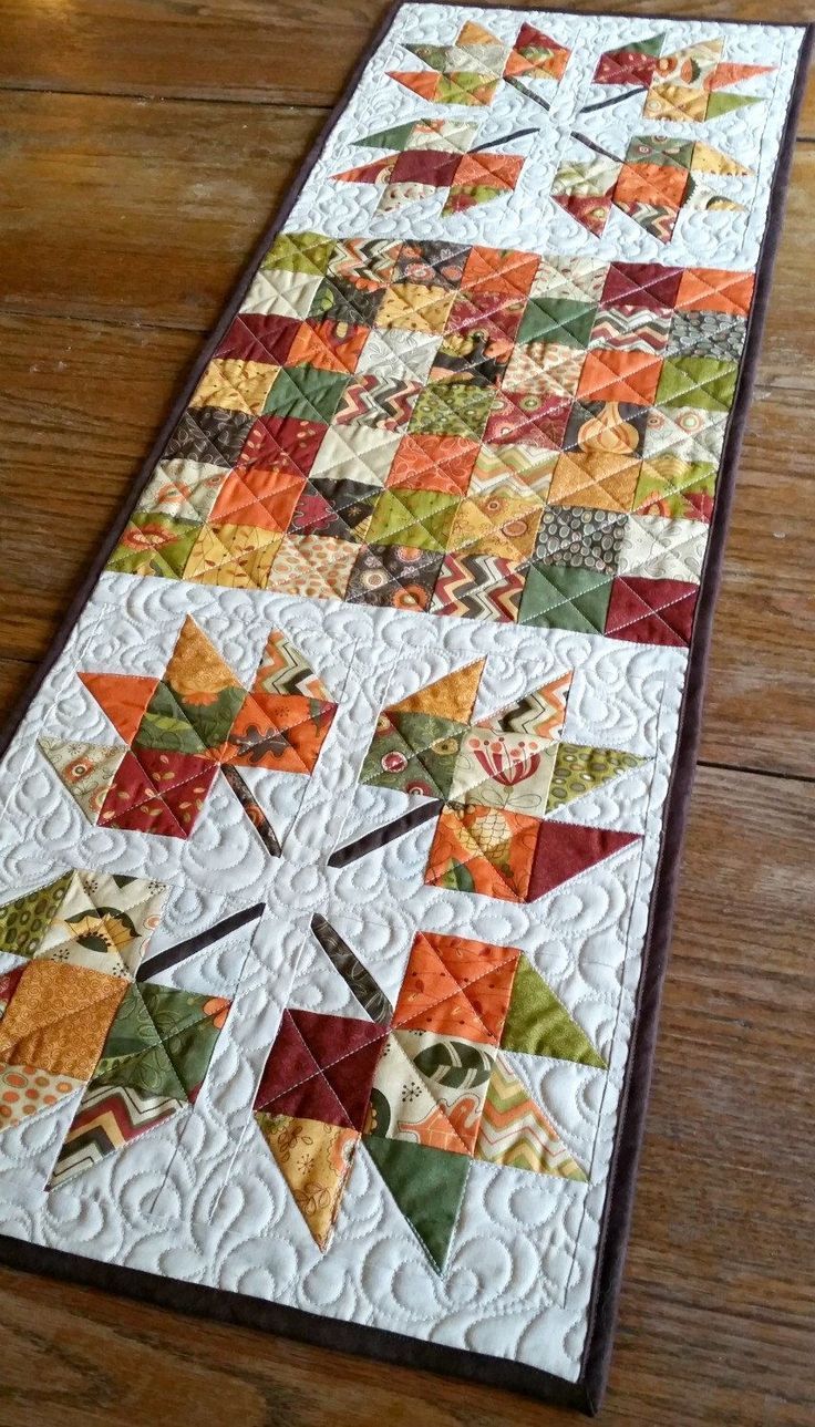 a quilted table runner on a wooden floor with an orange, yellow and green patchwork design