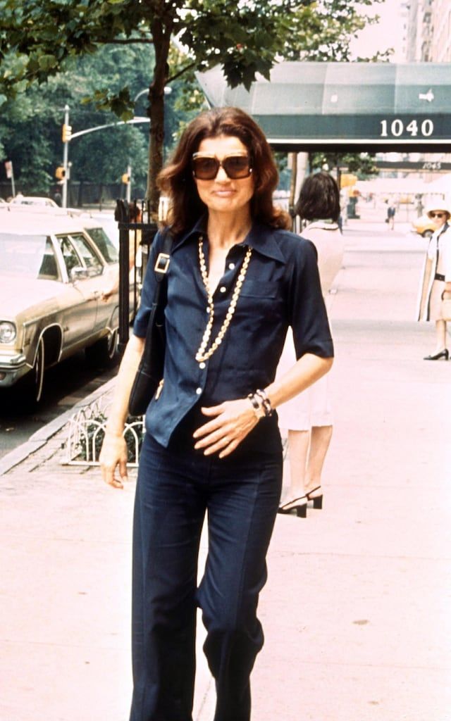 a woman walking down the street with her hand on her hip wearing sunglasses and a blue shirt