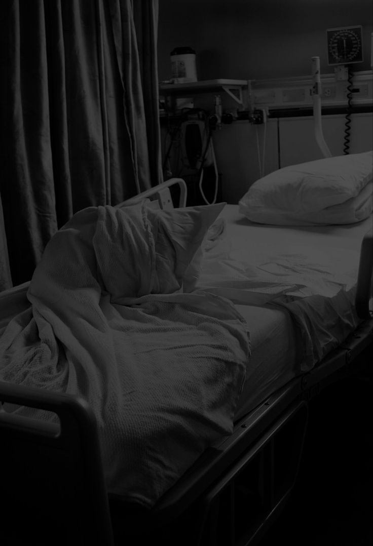 an empty hospital bed with white sheets and pillows on it, in a dark room