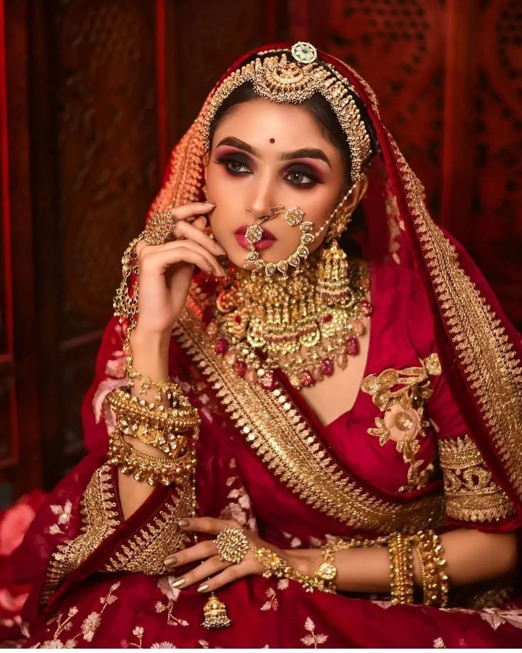 a woman in a red and gold bridal outfit with jewelry on her face, posing for